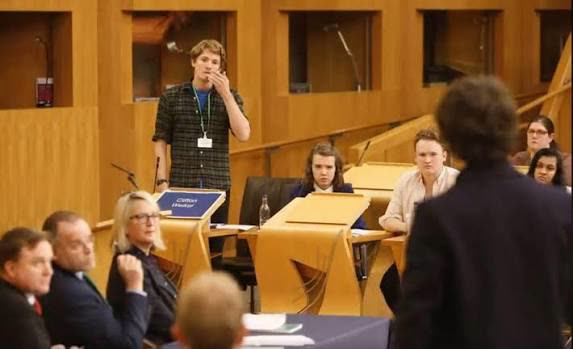 A student standing to speak in a schools debate held in a parliament chamber